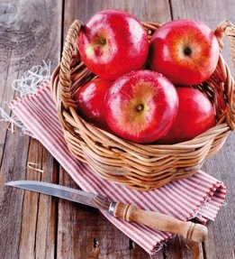 Healthy organic red apples in a straw basket and knife on a wooden background