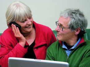 Coppia di anziani davanti ad un portatile che si guardano mentre la donna sta parlando al telefono